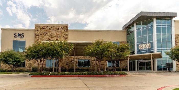 The Success On The Spectrum McKinney building at 6601 West University Drive, a stone and stucco office building with the SOS logo beside the entrance.