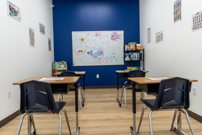 A closer view of the mock classroom, with a whiteboard drawing of sea creatures and a shelf of picture books beside the desks.