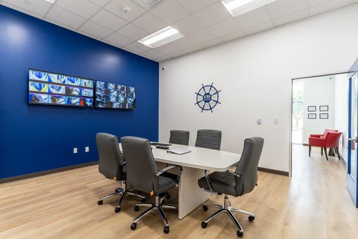 The parent viewing room at SOS McKinney: a meeting table facing two wall monitors showing live camera feeds from the therapy rooms.