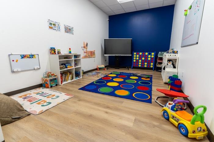 The playroom at SOS McKinney, with a circle-time rug, an interactive screen, a giant Connect Four, toy shelves and a calming corner with a beanbag.